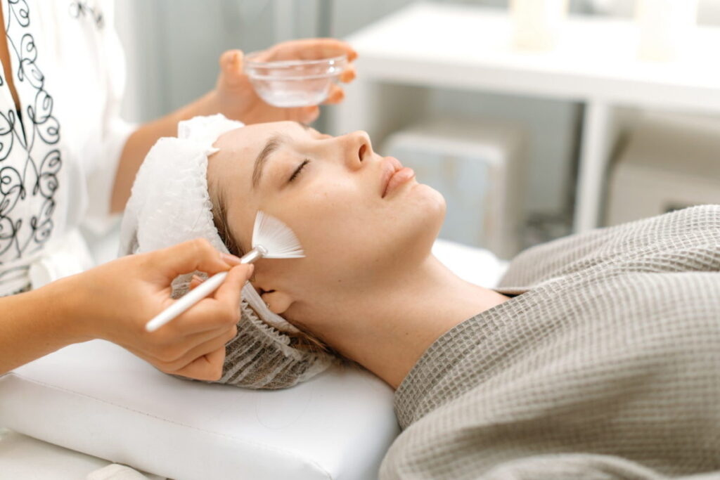 Beauty procedure. The cosmetologist cleans the face of a beautiful caucasian woman with special gel before applying a mask, peeling, scrub. Side view. Facial skin care procedures in a beauty salon