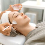 Beauty procedure. The cosmetologist cleans the face of a beautiful caucasian woman with special gel before applying a mask, peeling, scrub. Side view. Facial skin care procedures in a beauty salon